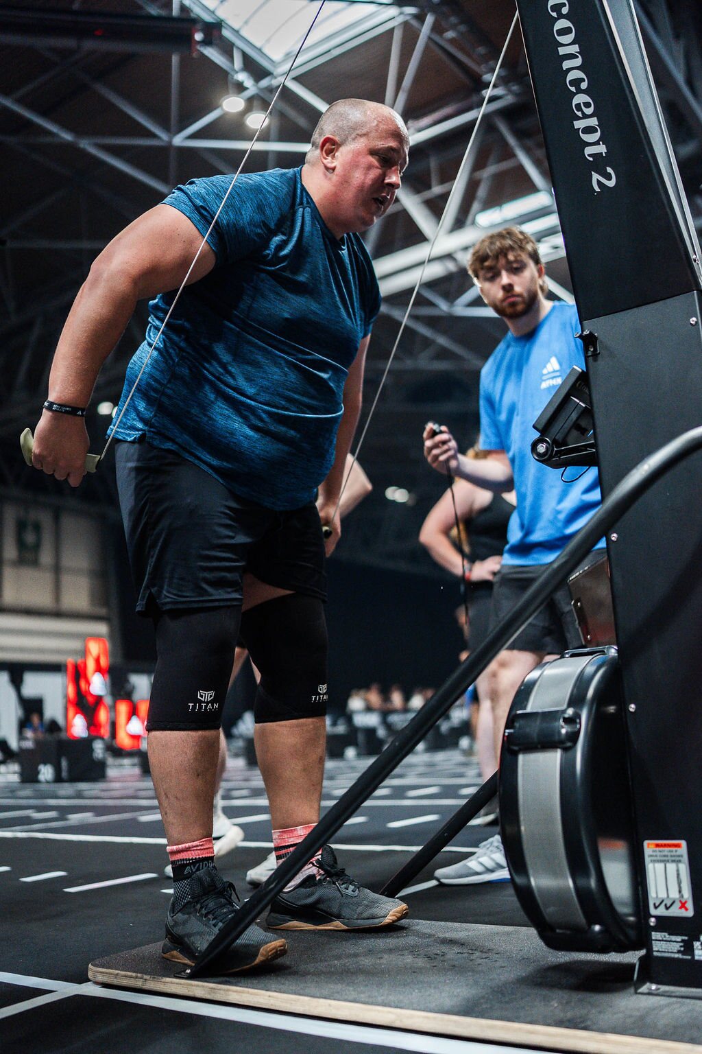 An athlete works hard on the Ski Erg while his judge keeps count